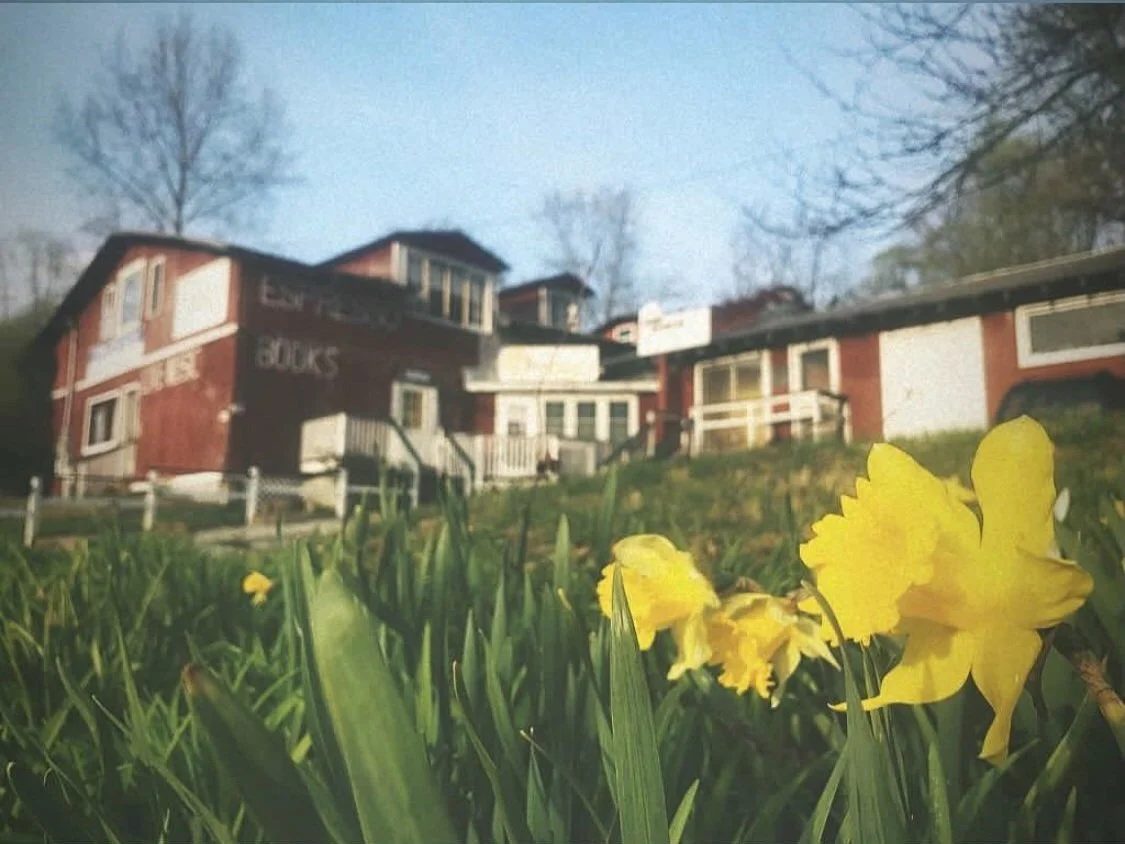 The barn-red Packing Shed on a spring day, ESPRESSO and BOOKS hand-painted in white on the siding, daffodils blooming in the foreground.